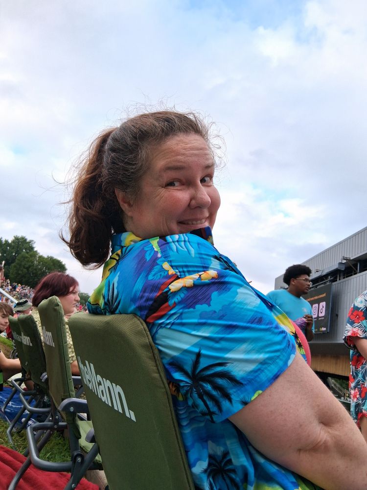 A smiling woman sitting in a camp chair at a concert. 