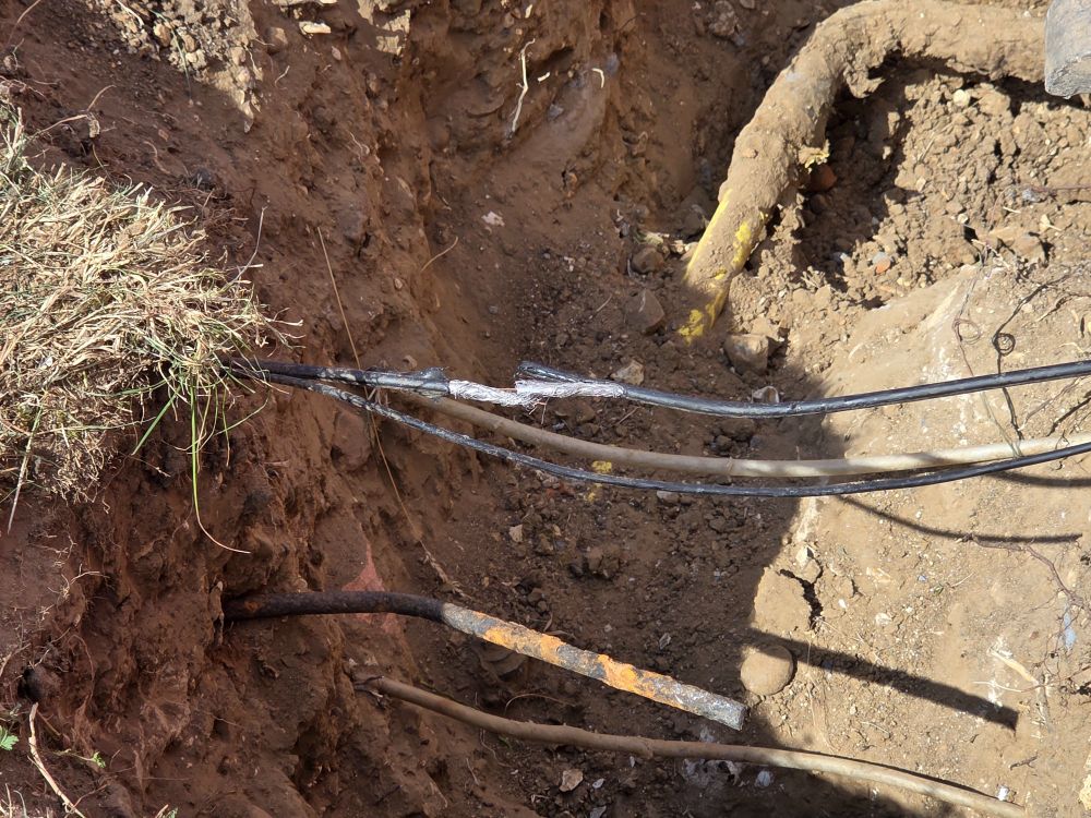 A trench with cabling running across the gap. One of the wires has been cut in two, and is exposed. 