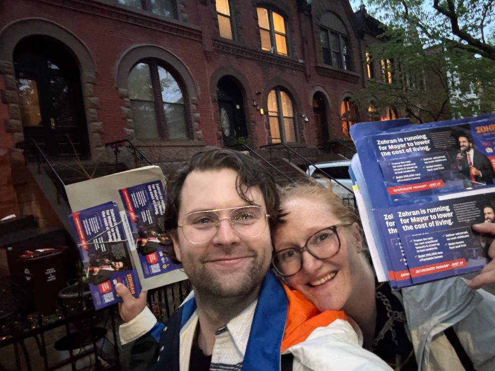 Couple in rainy weather in front of Brooklyn brownstones with Zohran Mamdani Flyers