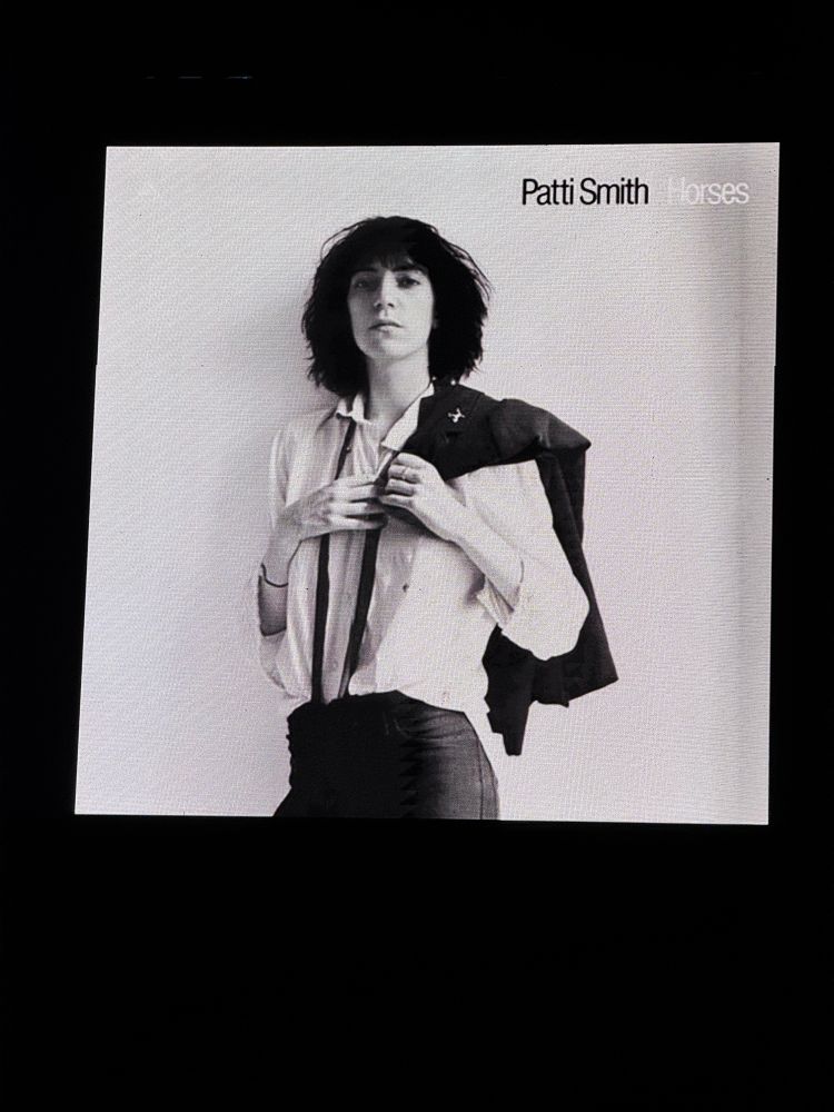 Concert venue screen showing cover of Patti Smiths Horses album