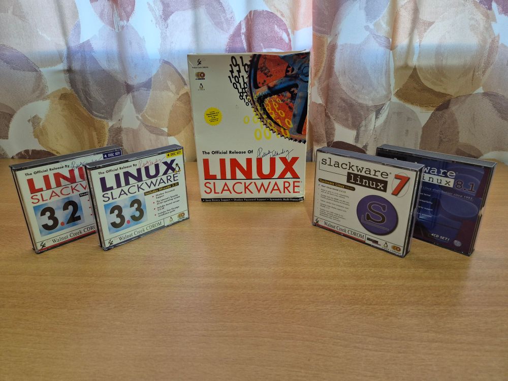 A box of software on a desk flanked on both sides by pairs of CD jewel cases, all containing versions of Slackware Linux.