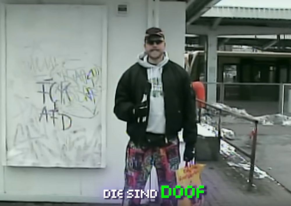 FiNCH steht vor einer Wand mit der Aufschrift FCKAFD, die Textzeile: "Die sind DOOF"