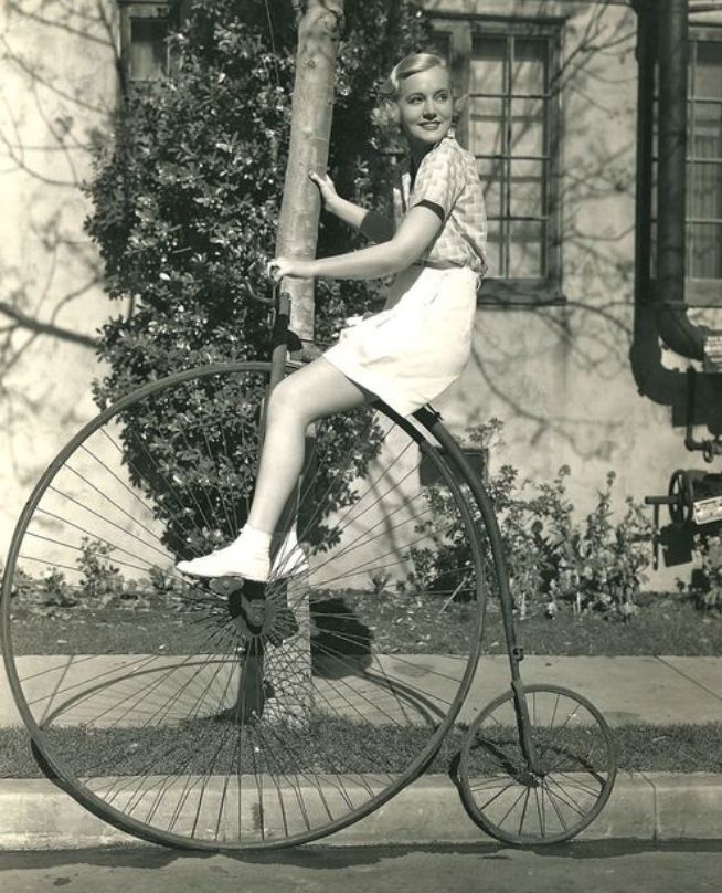 Black and white image of a woman sitting on a penny-farthing 
