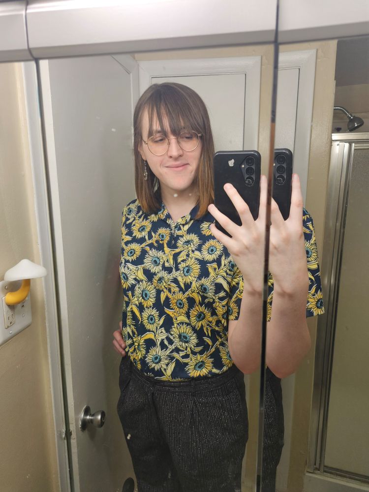 a grinning girl in a blue polo covered in sunflowers, tucked into waist-high slacks