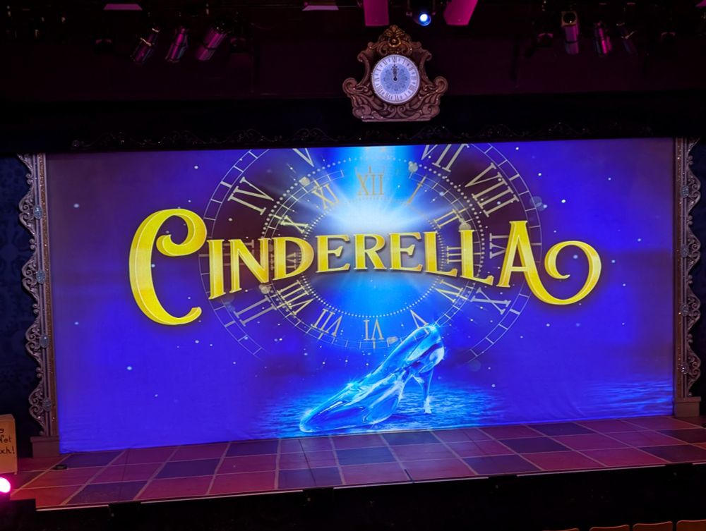 A photo of the theatre's stage with Cinderella projected on the front screen. There's an old time clock hanging central above the stage