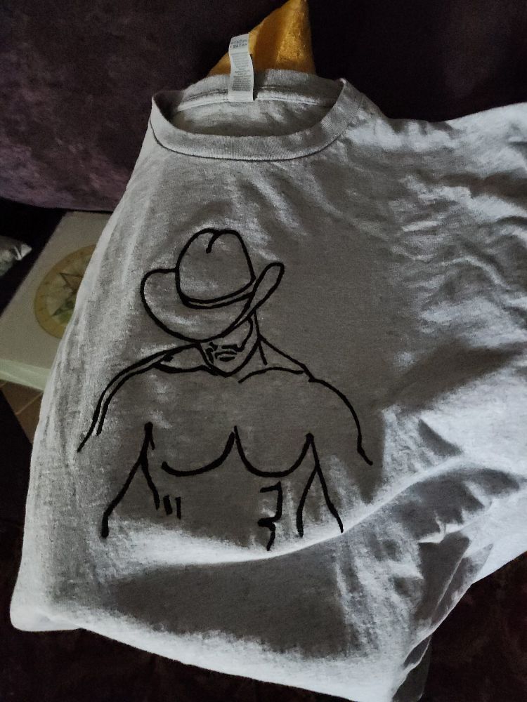 A grey t-shirt embroidered with a line art style drawing of a shirtless muscular cowboy torso.
