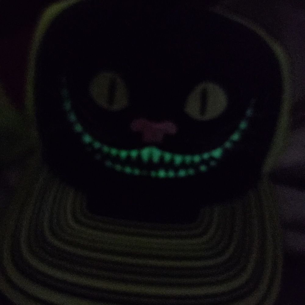 Teeth glowing from an embroidered hat with cheshire cat smile