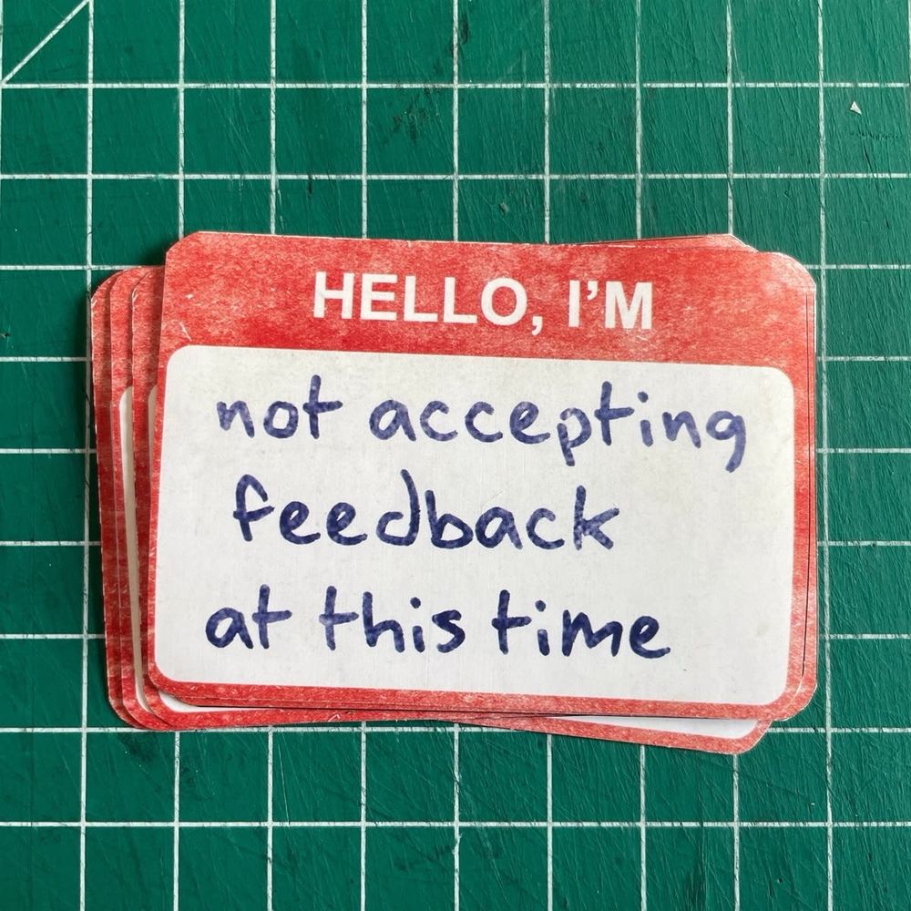 Photo of a name tag that says “hello, I’m not accepting feedback at this time” in sharpie marker 