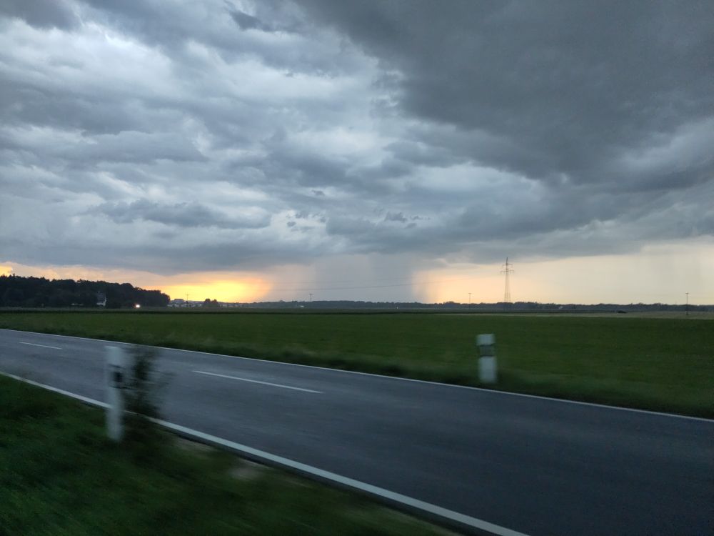 Eine Regen downpour, dahinter roter himmel, im Vordergrund eine Landstraße