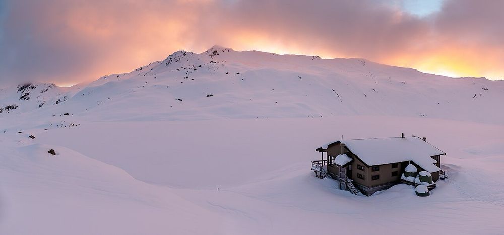Winter Angelus Hut with Angelus Lake behind it. Mountain peak in the distance. Photo taken at sunset. 