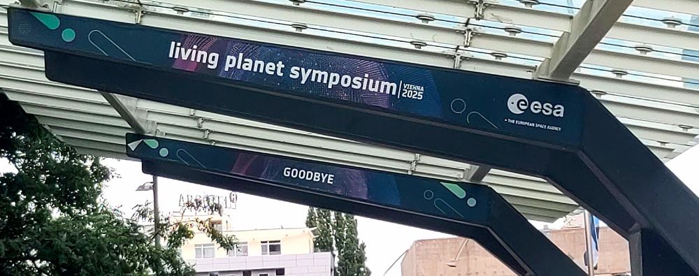 A roof-carriage over the path from the conference centre to a metro station, outfitted with signs saying "esa living planet symposium 2025" and "GOODBYE"