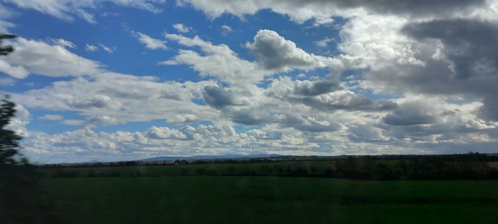 A blue sky covered with clouds, an open field of grass is in the foreground 