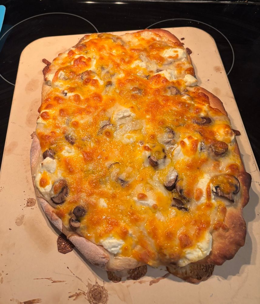 Pizza with goat cheese, cheddar, and mushroom on a pizza stone