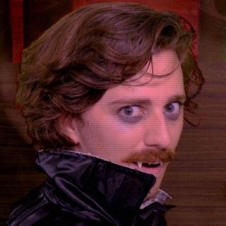 Brian David Gilbert dressed as a Dracula looking coyly over his Dracula shoulder as if to say, “who, me?”