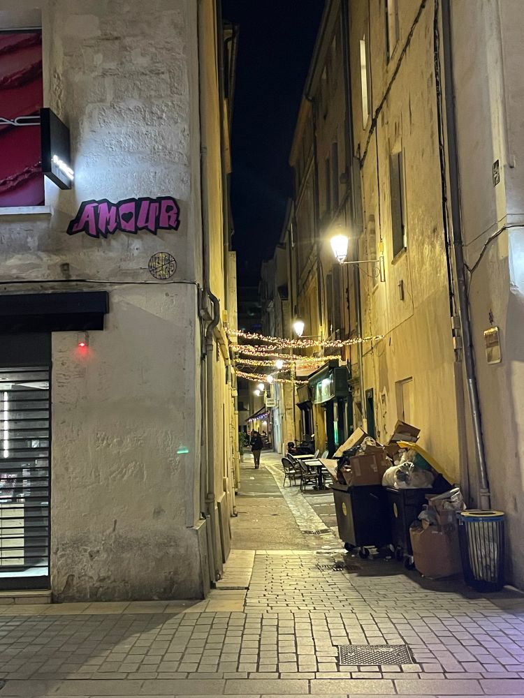 An alleyway in Montpellier’s old town. Street art on the wall reads “Amour”, while the alley ahead is lit with lights hanging from wires over the street 