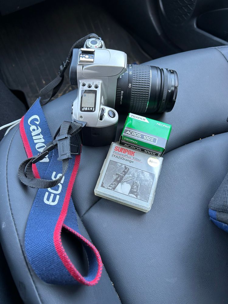A Canon Rebel 2000 film SLR camera, a roll of Fujifilm Acros 100 B&W film, and an orange contrast filter.