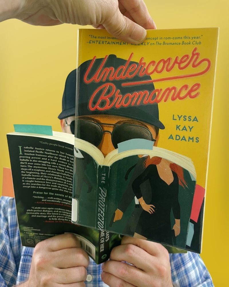 Bookface photo of staff member with the book “Undercover Bromance” by Jessica Lyssa Kay Adams. Bookface photos are when staff pose with a book cover to visually align themselves with the image on the cover, creating an optical illusion. 