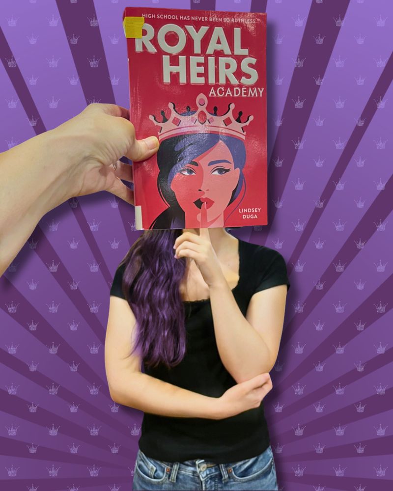 Bookface photo of staff member with the book “Royal Heirs Academy” by Lindsey Duga. Bookface photos are when staff pose with a book cover to visually align themselves with the image on the cover, creating an optical illusion.  