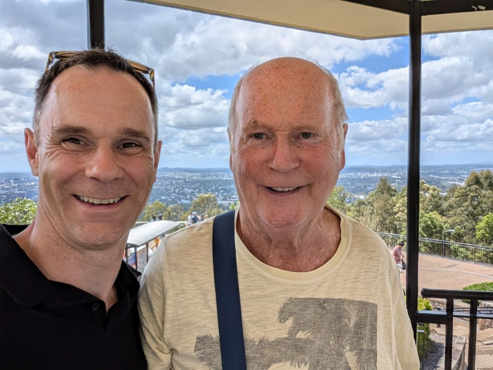 Neil Benson and his dad, Bert, on a hill top overlooking Brisbane City with a partly sunny sky.