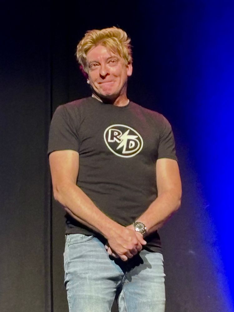 Rhys Darby clasping his hands and looking bashful at his show in Cardiff