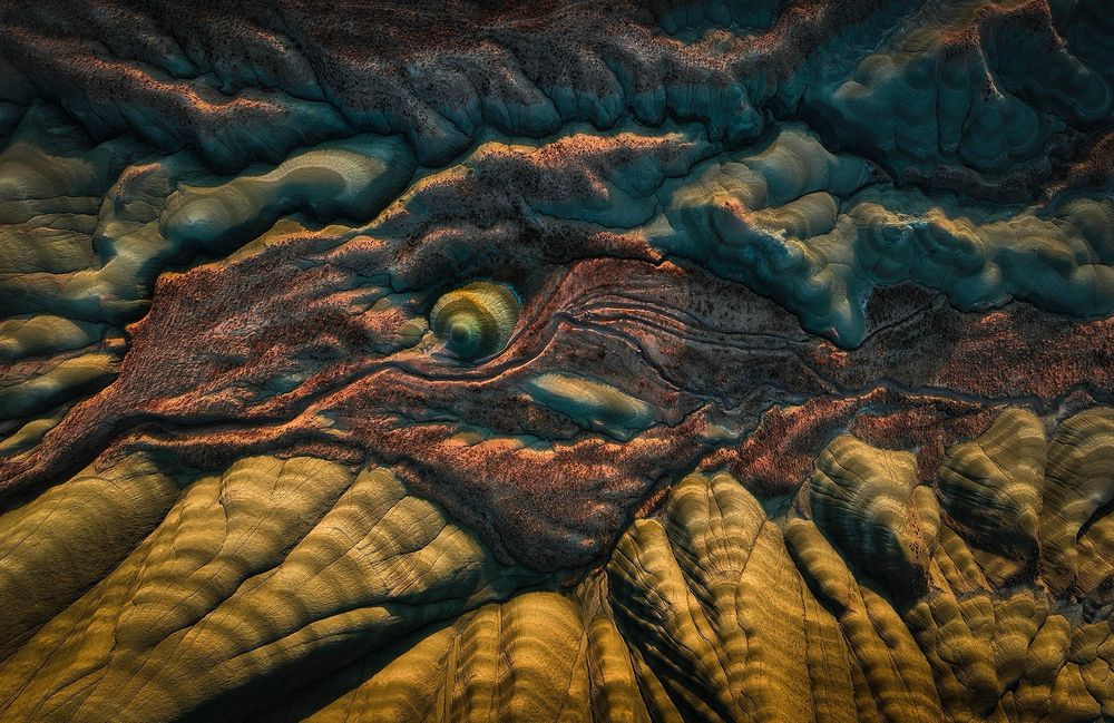 Top down view on some sand stone hills in Turkey. The morning light creates surprising contrast and reveals the different layers of colors. A dragon/dinosaur head shape appears from the patterns… 
Originally I had shot this image to be displayed vertically, but a good friend made me notice about that dragon head so I decided to display it horizontal to highlight it. 