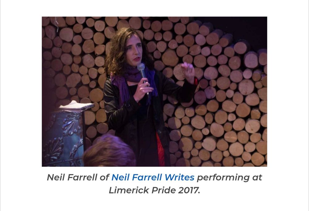 Neilly with long hair, makeup, a big purple scarf, delivering something emphatic over a microphone in a cosy indoor venue, 