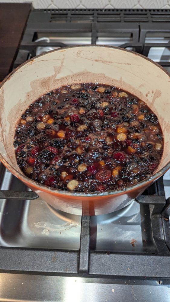 A pot of dark red, simmering liquid in which six different types of dried fruit float like red, orange, blue, and yellow jewels.