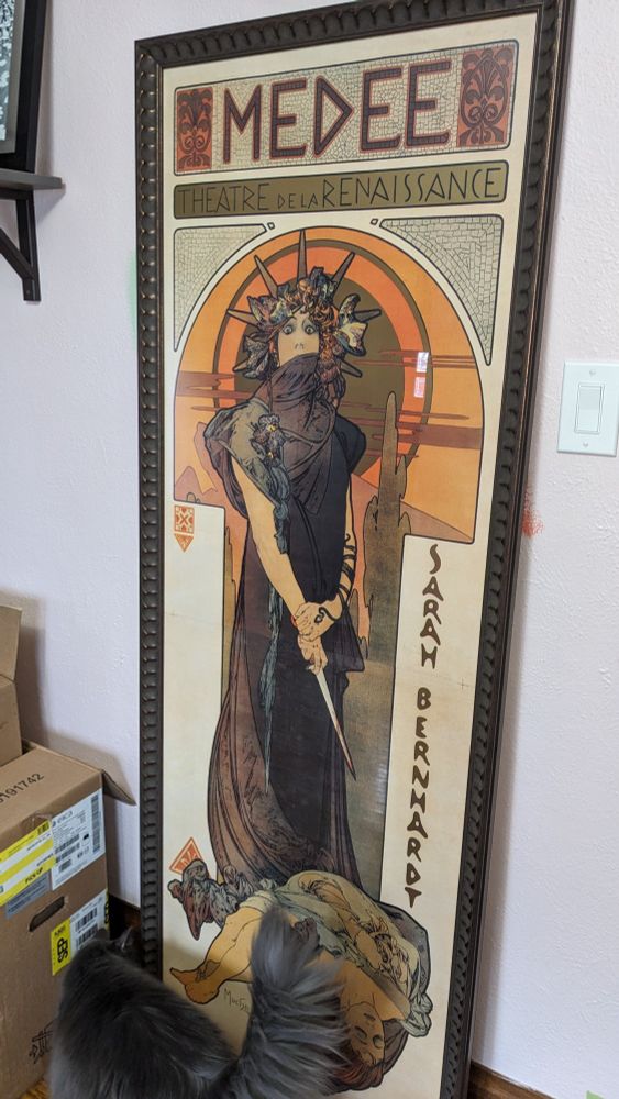 A framed poster of Mucha's "Medee", produced for the Sarah Bernhardt theatre production. Medea stands horrified with a bloody dagger over the bodies of her children. The framed print is six feet tall.