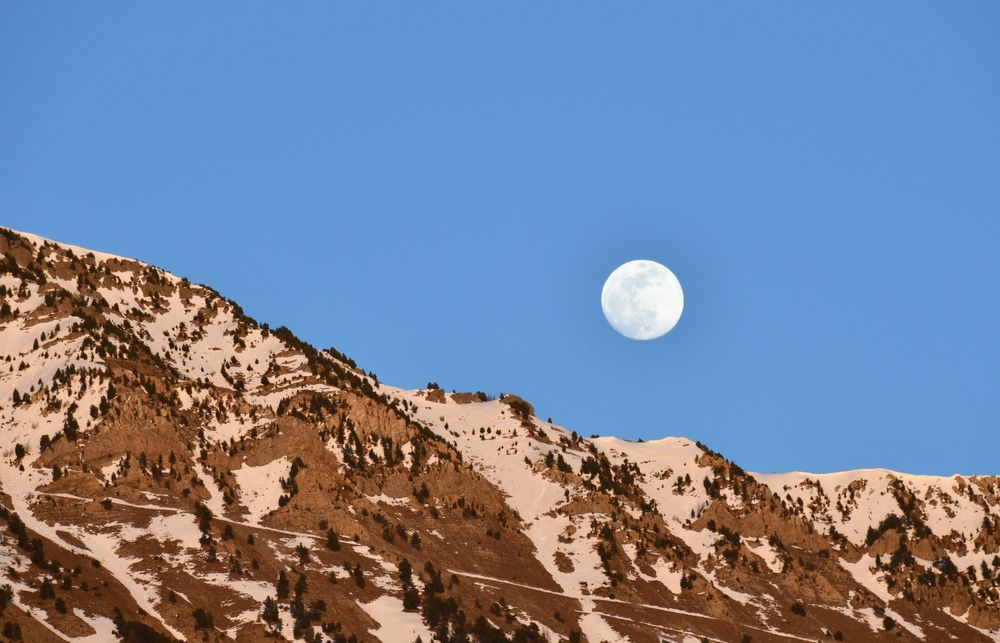 Pleine lune se levant en soirée sur des montagnes enneigées. 