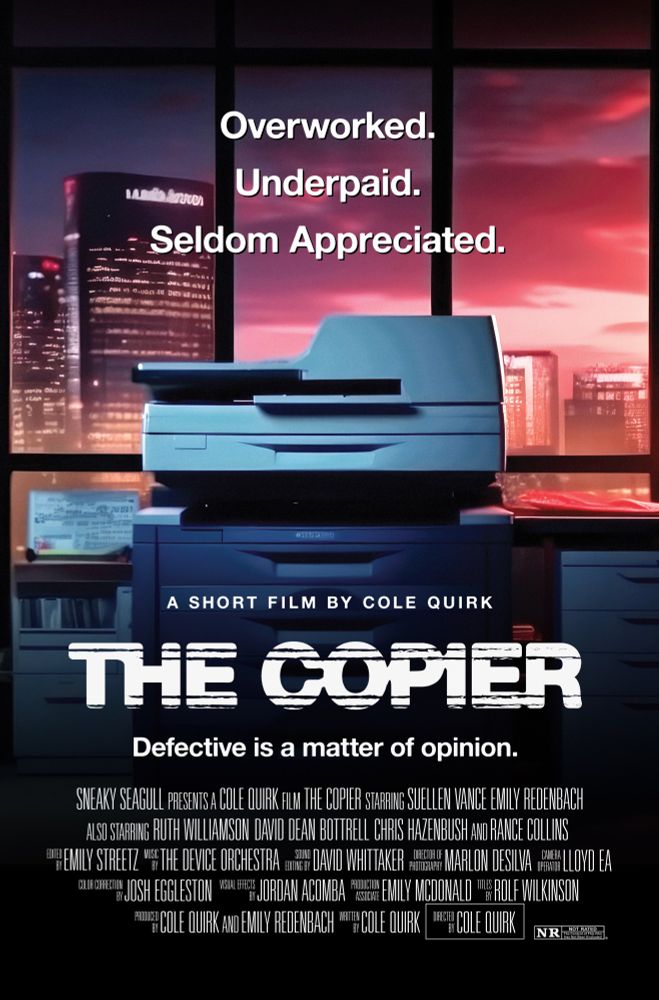 A movie poster with a copier on it, in an office building, in front of a window showing a sunset.