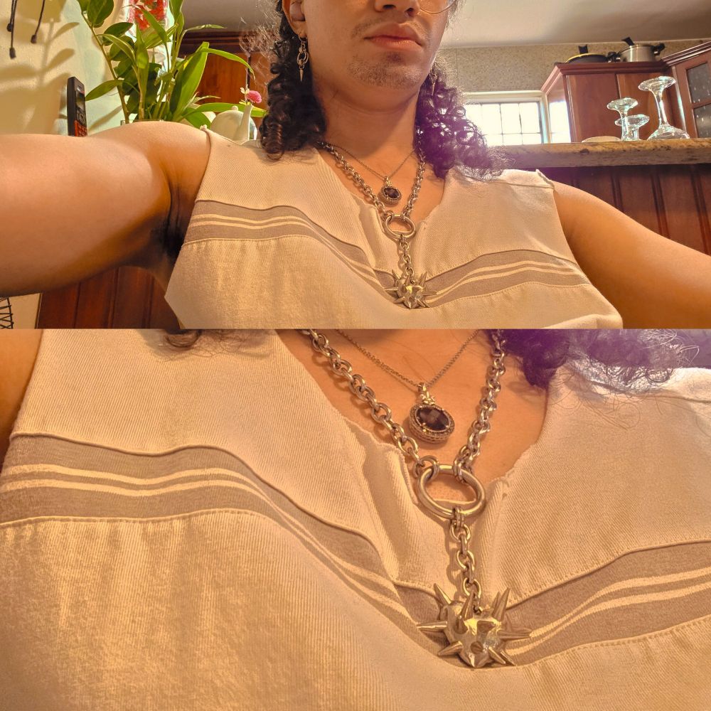 Young nonbinary AMAB with curly hair posing sensually with armpit hair visible, and face partially visible from the nose down. They are dressed in grey sleeveless shirt and wearing a spiky heart chain necklace.