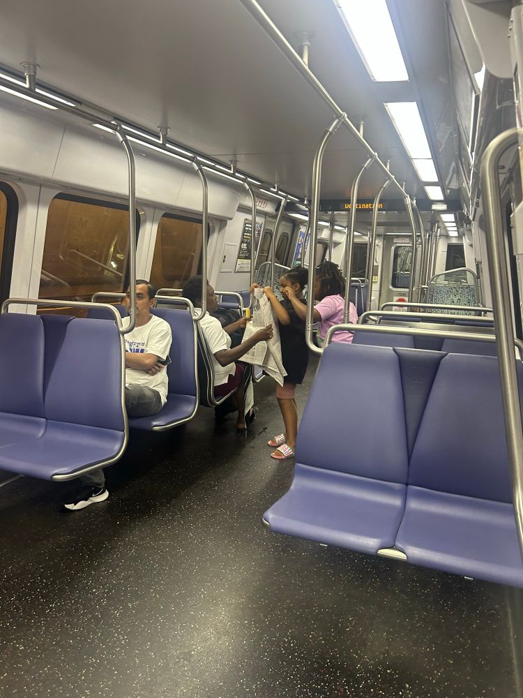 Two little girls with their mom on the metro looking at the newspaper 