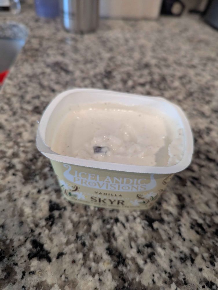 Photo of a newly opened cup of Icelandic Provisions vanilla skyr with a small piece of dark brown glass in it.