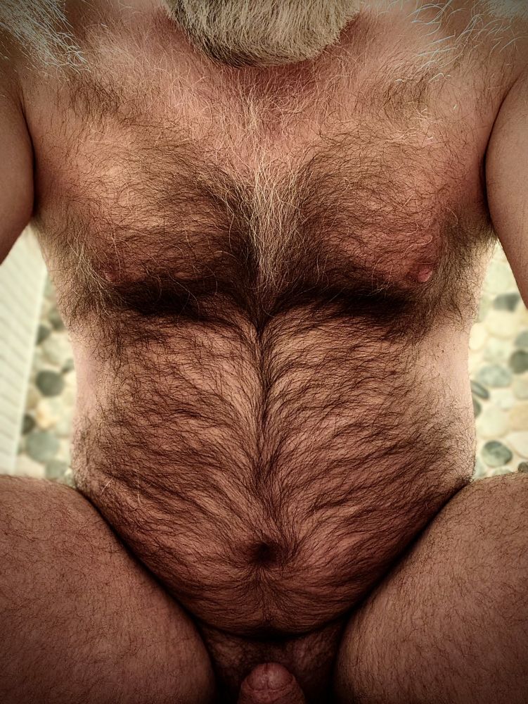 Hairy bearded nude man sitting and showing his belly and chest. Tip of his hard dick is visible too. Color image