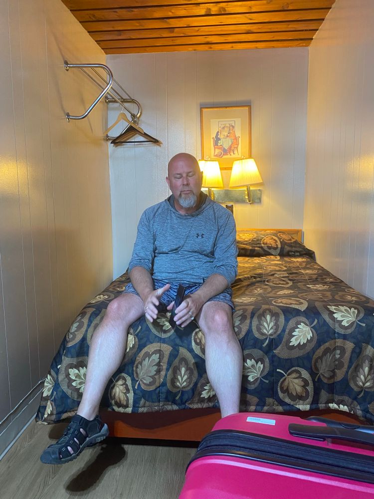 Dave on a terrible bed in a terrible motel in Prince Rupert. His expression is tired and exasperated. I was laughing myself silly. 