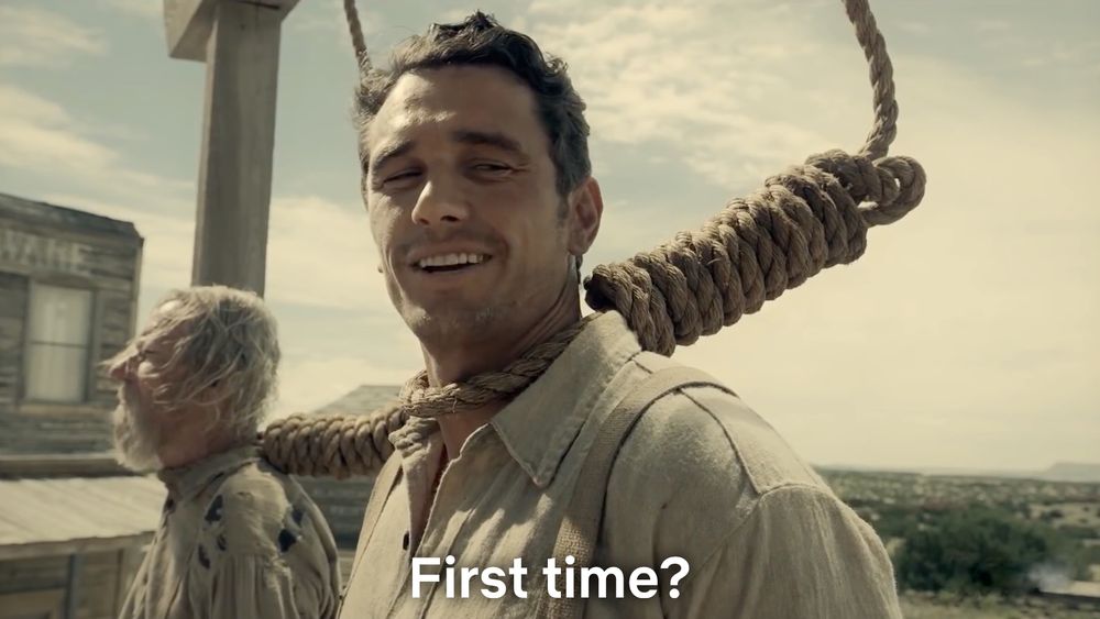 Screenshot from the Ballad of Buster Scrugs, man with a noose around his neck smiling and speaking to the person next to him on the gallows saying “First time?”