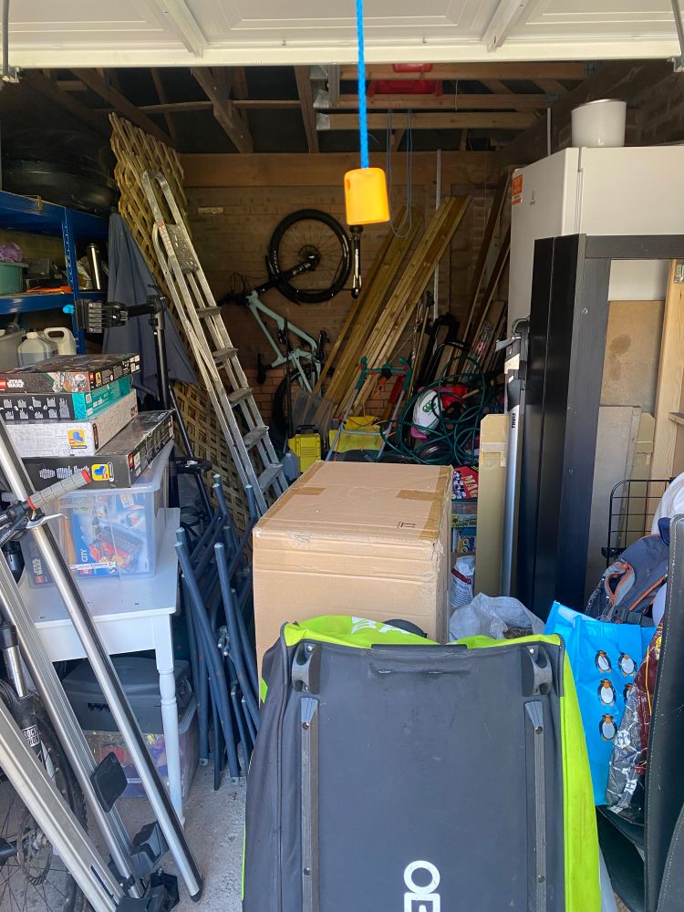 A garage absolutely packed full of shit, with a bike just barely visible at the far end, hanging on the wall.