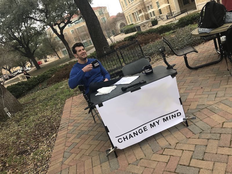 Man drinking coffee in front of a "change my mind" sign.
