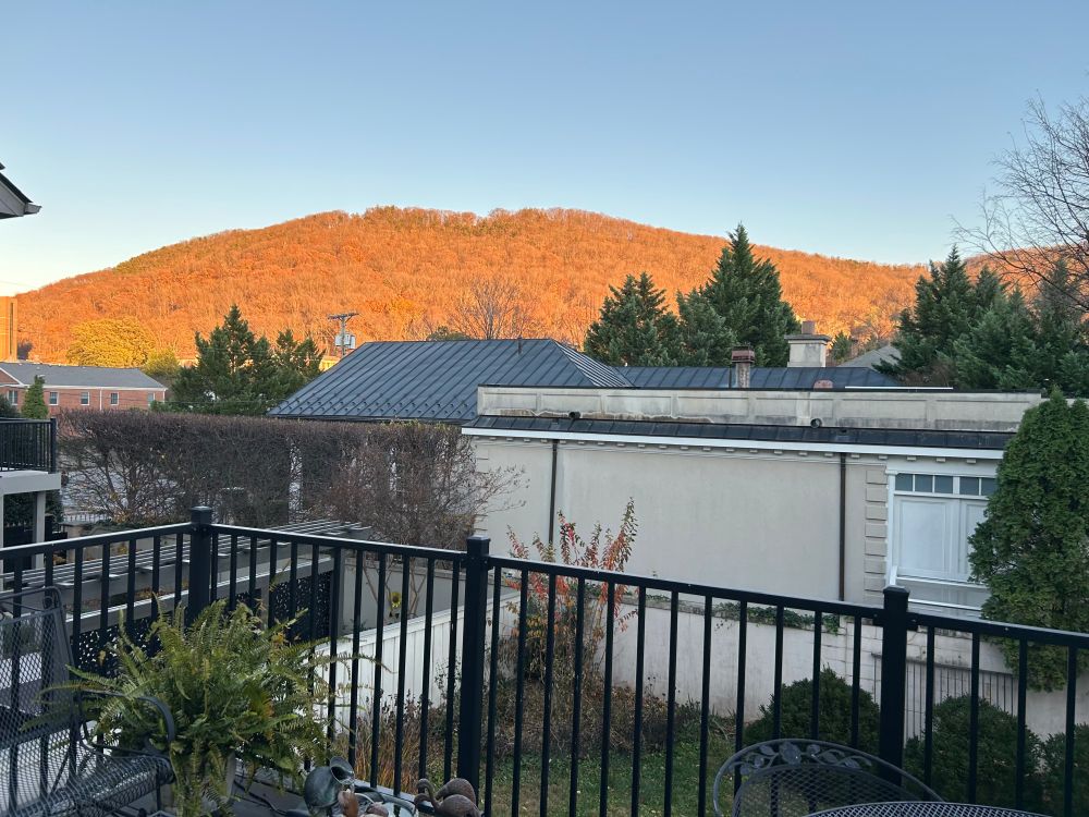 In the foreground, a balcony. In the background, a mountain whose trees are at peak fall color-orange.
