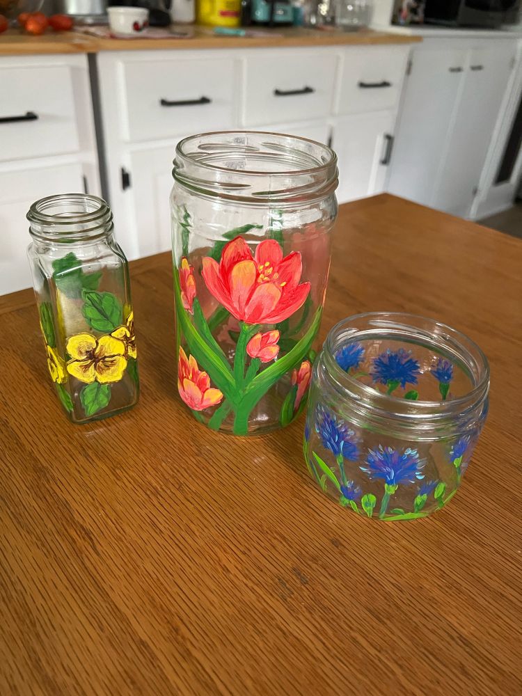 Three reclaimed glass jars of different sizes and shapes painted with pansies, tulips, and blue bonnets.