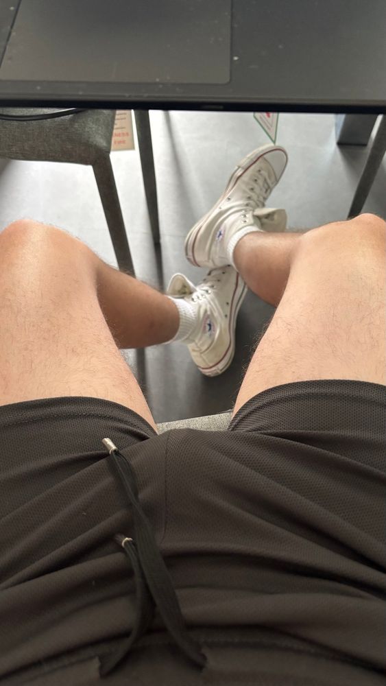 Men’s legs wearing white converse and white socks. Bulge in gym shorts 