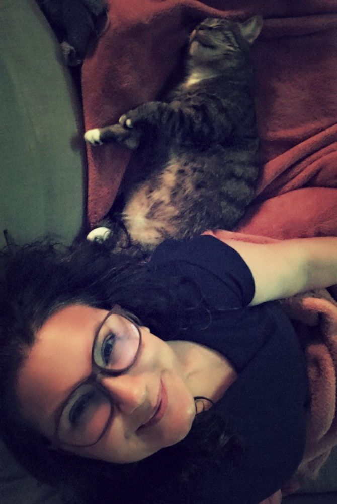 me sitting next to my cat who is passed out belly up on the couch