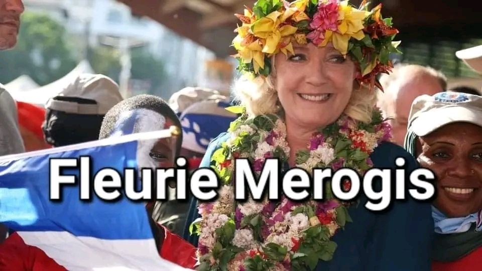 Marine Le Pen avec un collier et couronne de fleurs qui sourit, en dessous il y a écrit 
Fleurie Merogis