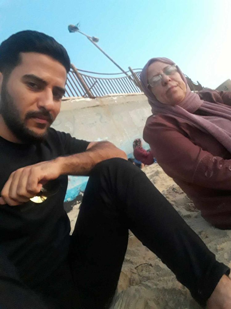 Photo d'Ahmad et sa maman, assis sur du sable et dos à un muret