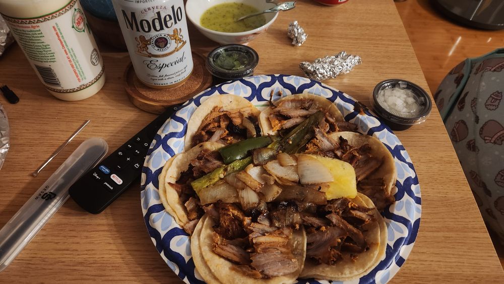 6 pork tacos with a chili pepper, onions and pineapple. There is a Modelo and sauces on the side.