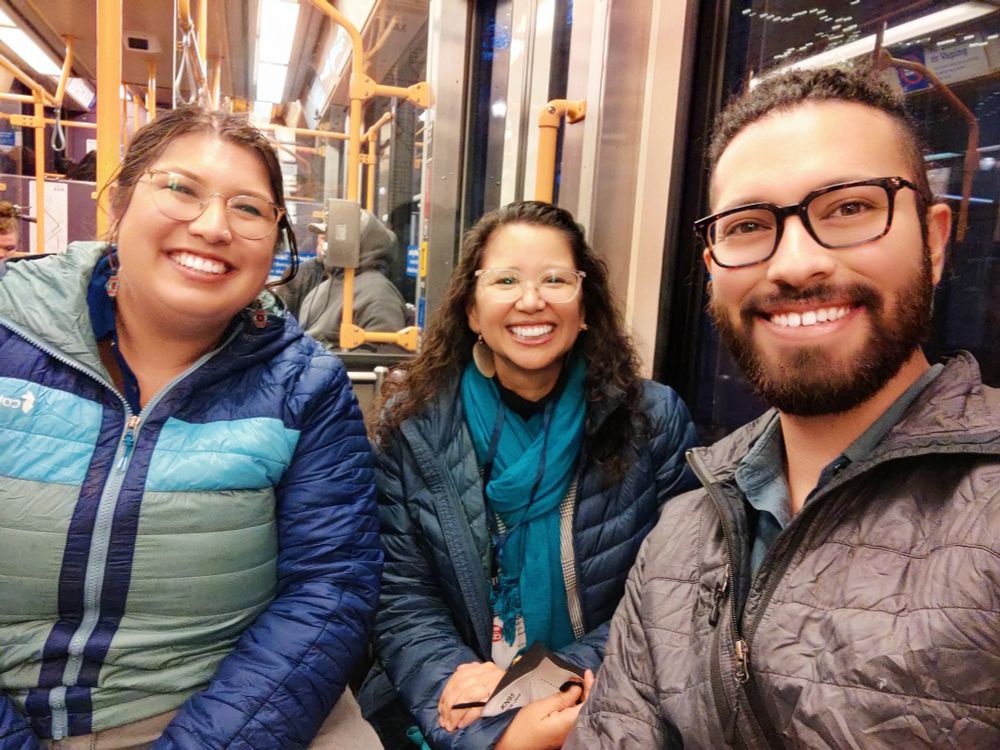 Three people sitting in a train smiling, two students and Katy Pinto in the middle