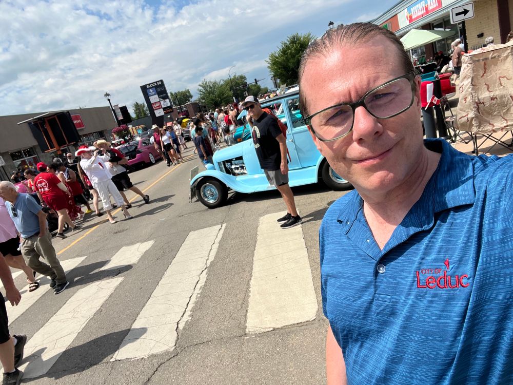 Councillor Ryan Pollard standing on 50th Avenue, Leduc. A crowd of people at the car show in the background