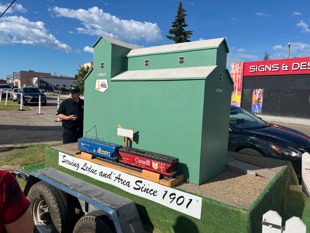The Leduc Legacy Heritage Society grain elevator parade float. There is a model of a green grain elevator marked “Alberta Wheat Pool,” and Alberta and Canada grain railway cars.