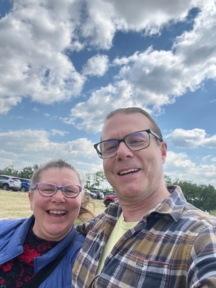 Councillor Ryan Pollard and Cindy Danyluk-Boisvert standing in a field, fluffy clouds in the background
