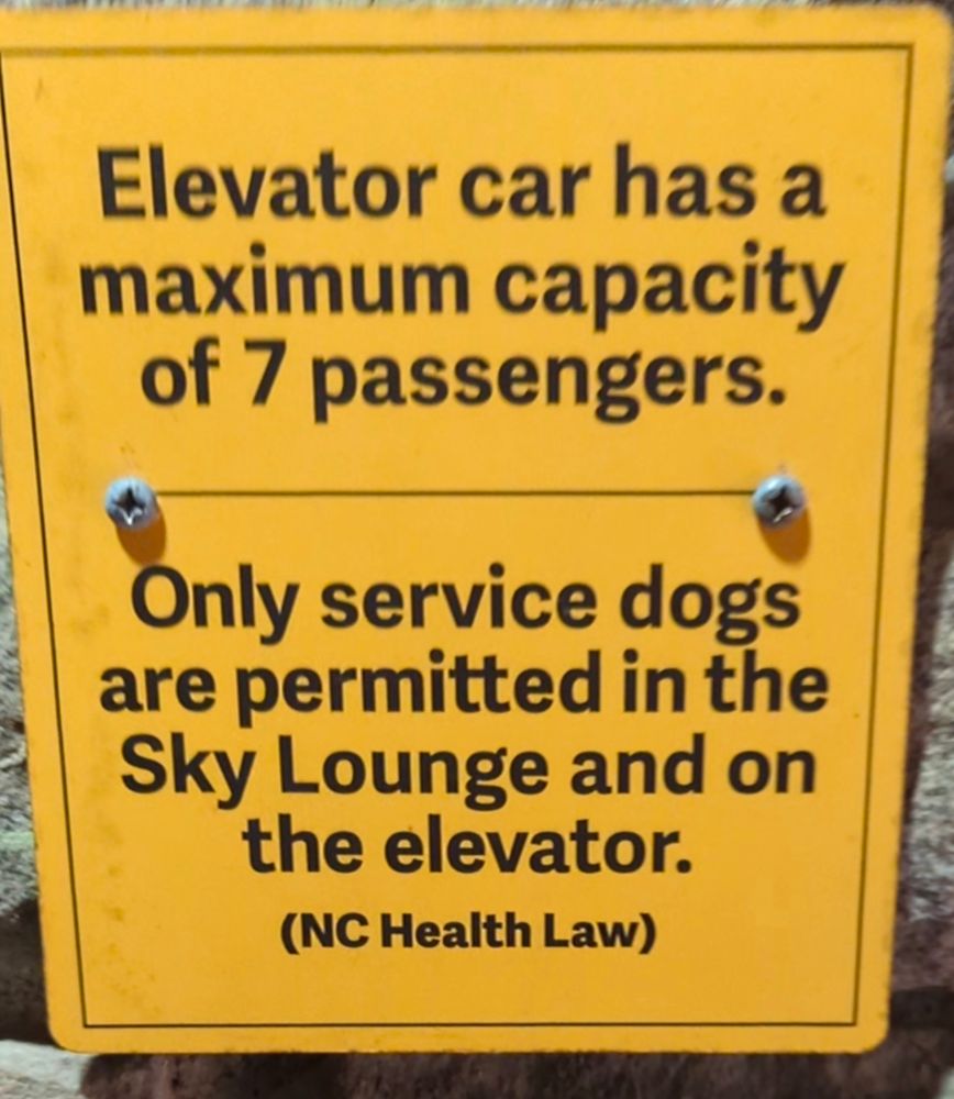 Sign says "Elevator car has a max capacity of 7 passengers. Only service dogs are permitted in the sky lounge and on the elevator.